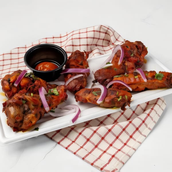 Spicy chicken lollipops with red onion slices and dipping sauce on a white platter.