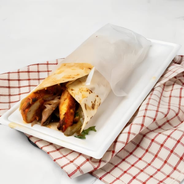 A chicken shawarma wrap, partially unwrapped, on a white plate with a red and white checkered napkin.